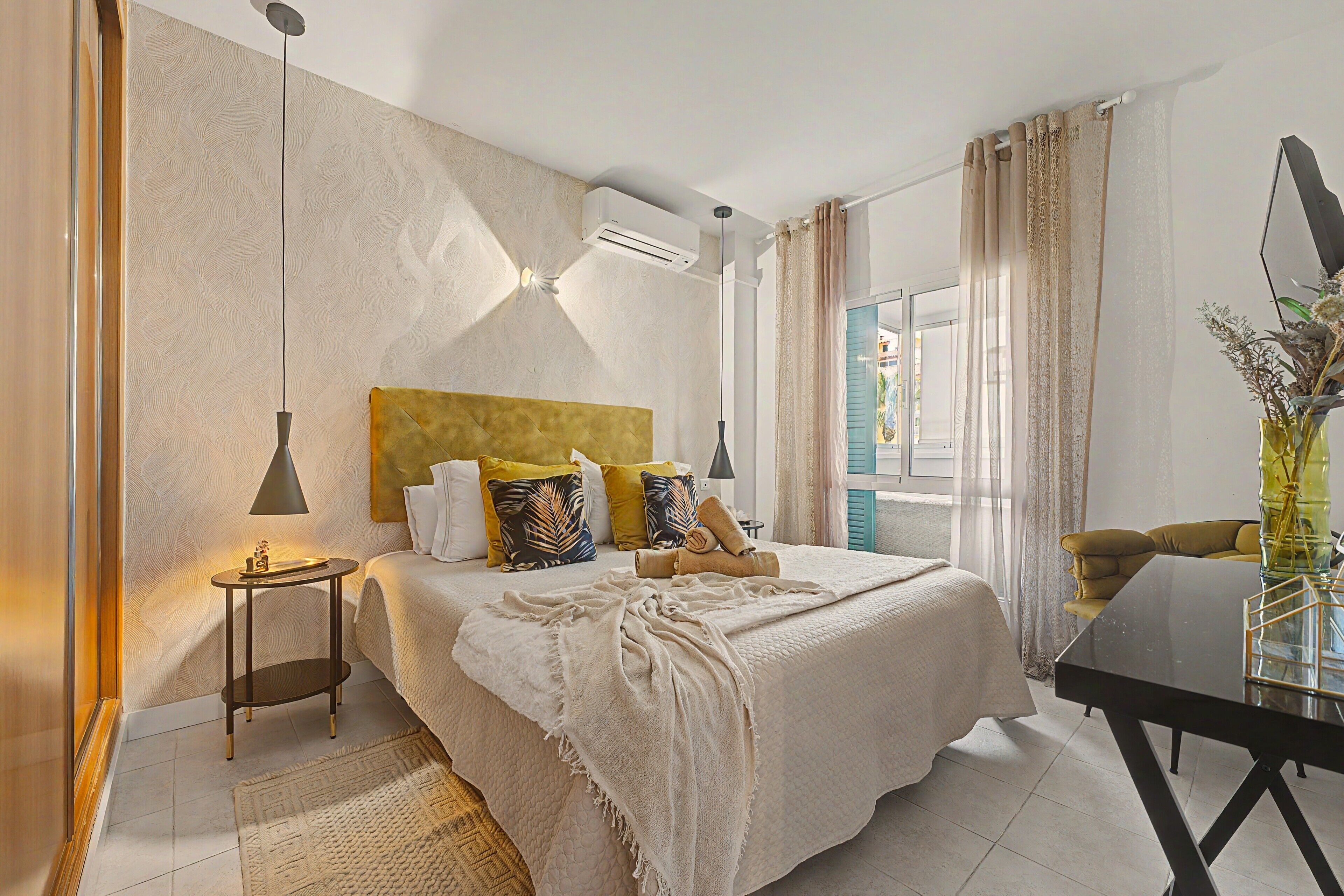 Habitación de hotel con cama, mesita de noche, lámpara y vistas al exterior.