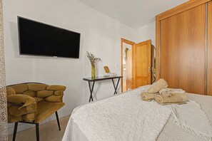 A bedroom with a bed, a chair, a desk, a television, and a wardrobe. - Apartment 'Reserva Del Higuerón' with Sea View, Wi-Fi and Air Conditioning (Fuengirola)