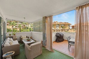 Ein Balkon mit Korbmöbeln, einem Grill und Blick auf eine Wohngegend.
