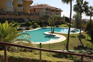 A swimming pool with a curved design, surrounded by palm trees and a building with balconies. - Apartment 'Reserva Del Higuerón' with Sea View, Wi-Fi and Air Conditioning (Fuengirola)