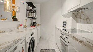 Una cuina moderna amb rentadora integrada, cafetera i microones sobre un taulell de marbre blanc.