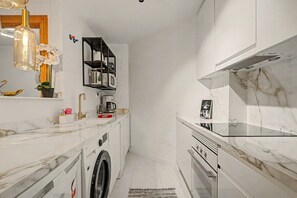 A modern kitchen with a built-in washing machine, a coffee maker, and a microwave on a white marble countertop. - Apartment 'Reserva Del Higuerón' with Sea View, Wi-Fi and Air Conditioning (Fuengirola)