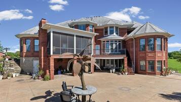 A large brick house with a spacious patio, a covered outdoor seating area, and a large windowed front section.