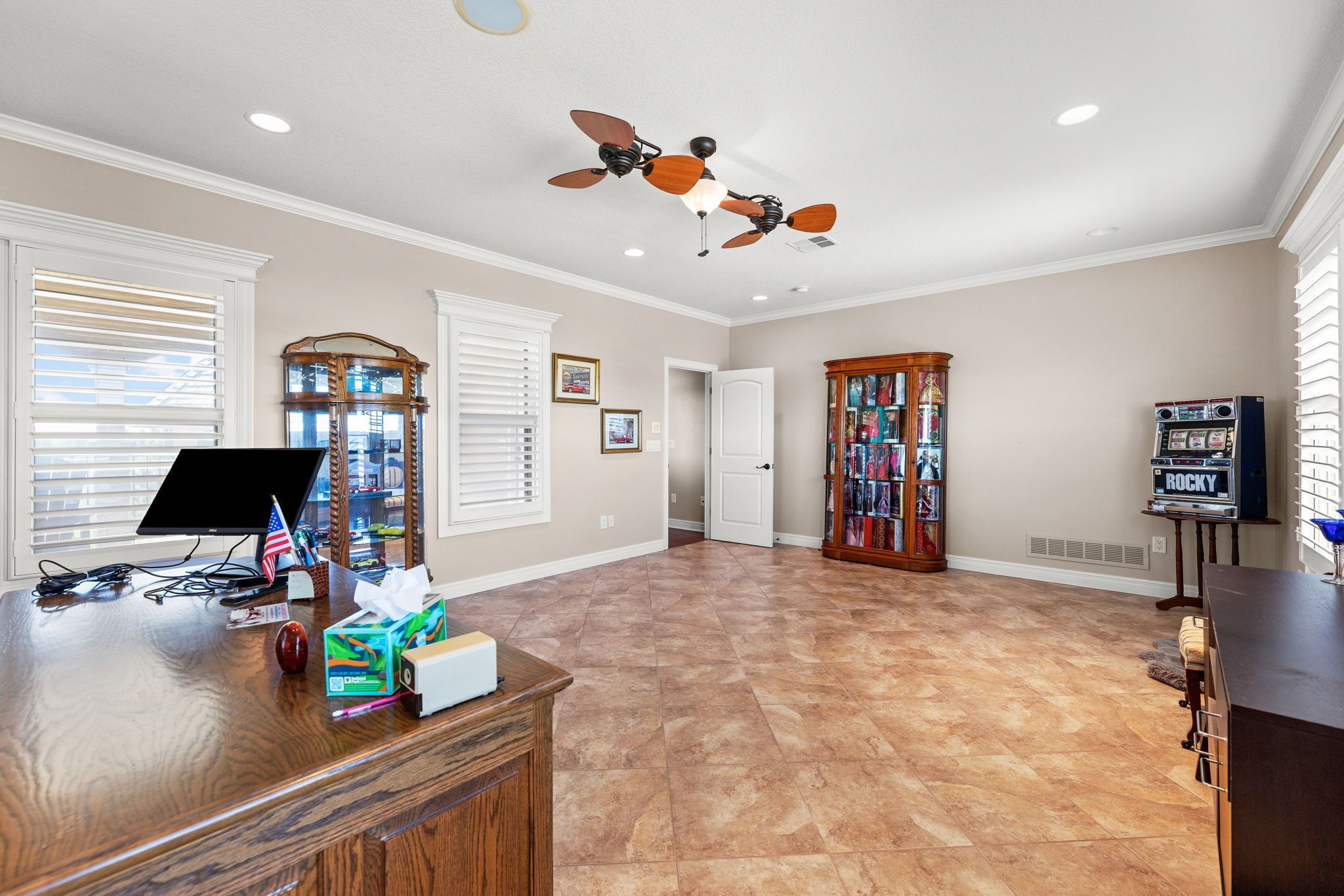 A spacious room with a wooden desk, a ceiling fan, and a bookshelf.
