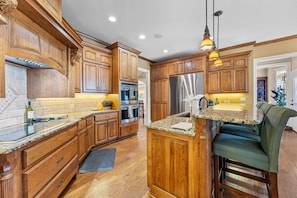 A kitchen with wooden cabinets, a stainless steel refrigerator, granite countertops, and a bar stool.