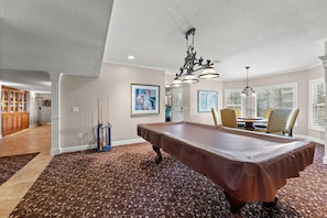 Una habitación amplia con mesa de billar, candelabro y alfombra estampada.