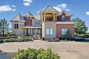 A large, multi-story house with a stone facade, multiple chimneys, and a spacious front yard.
