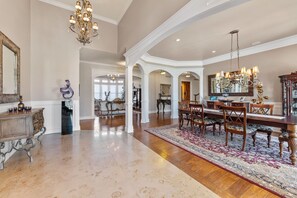 A spacious dining area with a large wooden table, chairs, and a chandelier.
