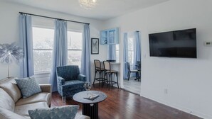 Een woonkamer met een bank, fauteuil, een eethoek en een tv aan de muur.