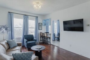 A living room with a sofa, armchair, dining area, and a TV mounted on the wall. - 1BR The Montrose W Main 06. Downtown, Med Center (Houston)