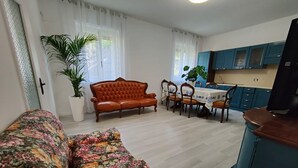Ein Wohnzimmer mit Sofa, einem Esstisch mit Stühlen, einer Küchenzeile und einem Fernseher.