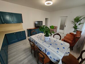 A dining area with a table covered in a floral tablecloth, surrounded by wooden chairs.
