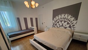 Ein Schlafzimmer mit Bett, Sitzbank, Nachttischen, einer Wand mit Muster und einer Chandelier.