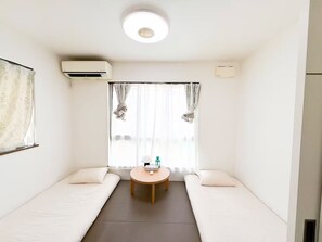 Ein Zimmer mit zwei Einzelbetten, einem kleinen runden Tisch, einer Klimaanlage und einer Deckenleuchte.