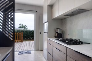 Una cocina moderna con estufa a gas, refrigerador y vistas al exterior por medio de una puerta corrediza.