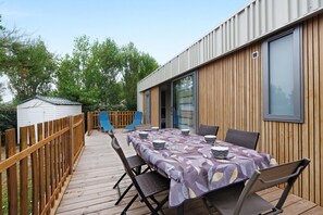Una terraza con mesa lista para comer, sillas exteriores y una cerca de madera.