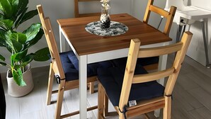 Un coin repas avec une table en bois, des chaises, une plante en pot et un téléviseur à écran plat fixé au mur.
