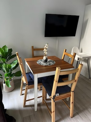Ein Essbereich mit Holztisch, Stühlen, einer Zimmerpflanze und einem an der Wand befestigten Flachbildfernseher.