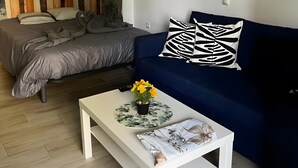 Un salon moderne avec un lit, un canapé bleu, une table basse blanche et un mur orné d’œuvres d’art abstraites.