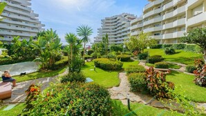 Un immeuble résidentiel doté de nombreux balcons, d’un jardin bien entretenu avec diverses plantes et d’un ciel dégagé.