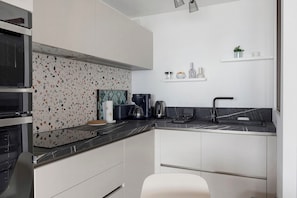 Una cocina moderna con encimera negra, armarios blancos y salpicadero con diseño moteado.