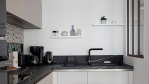 Una cocina moderna con encimera negra, pileta de acero inoxidable y alacenas blancas. Hay repisas sobre la encimera con diversos utensilios de cocina.