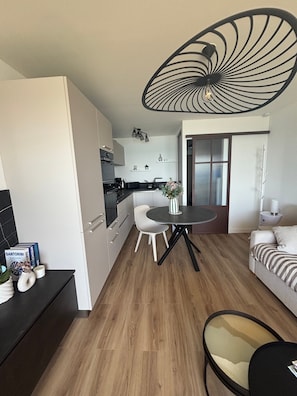 Una cuina moderna amb armaris blancs, una zona de menjador amb taula rodona i un saló amb sofà.