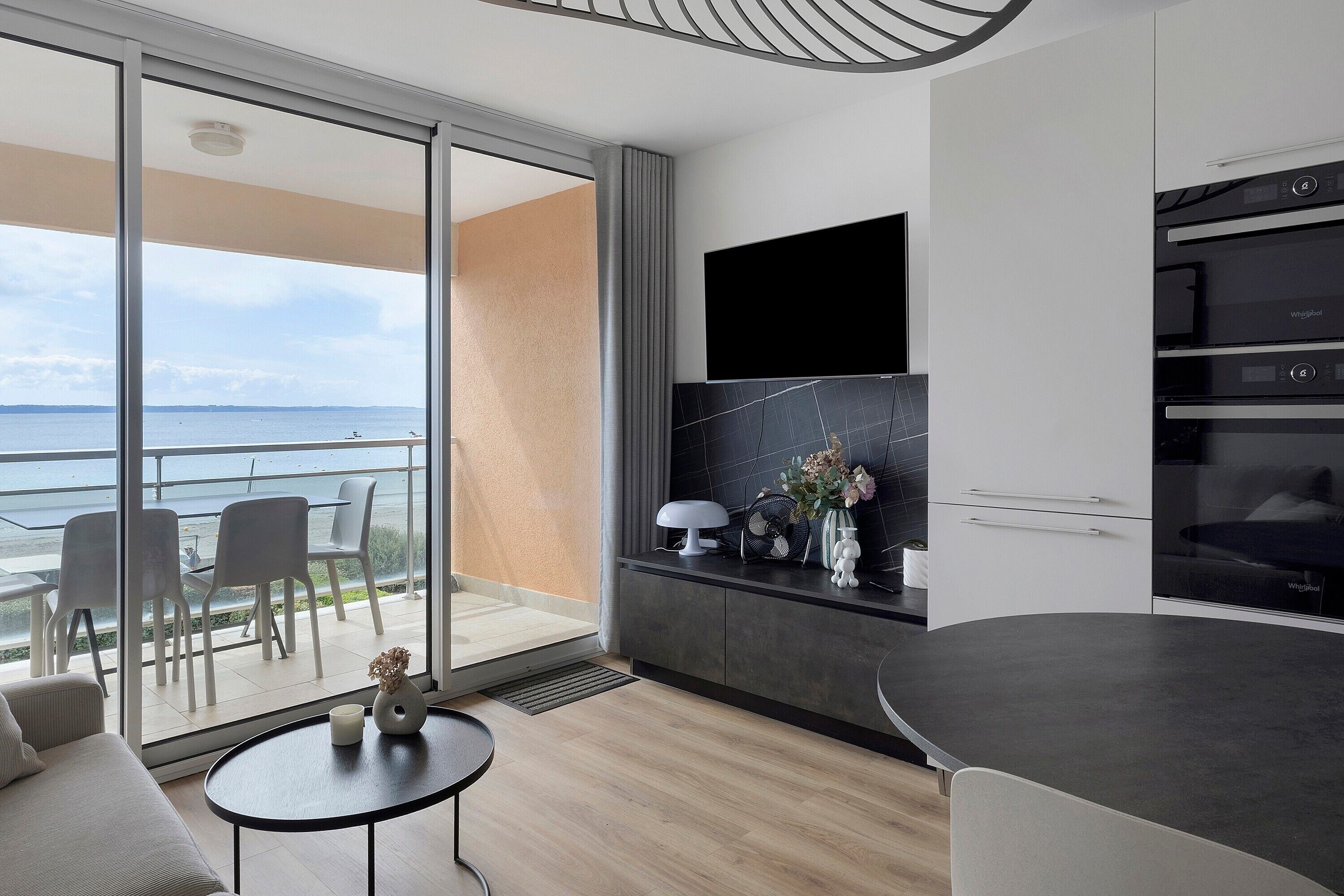 Eine moderne Küche mit eingebautem Ofen und einem großen Fenster, das auf einen Balkon mit Meerblick blickt.