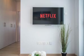 Un soggiorno moderno con una televisione a schermo piatto montata a parete che mostra 'NETFLIX', una pianta in vaso e un pavimento in legno.