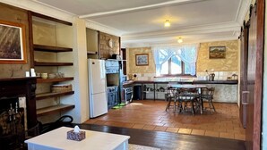 Amplia sala de estar con chimenea, comedor con mesa y sillas, cocina con refrigerador, estufa y lavaplatos, y un ventanal con cortinas.