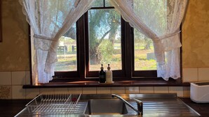 Una cocina con un lavamanos, un escurreplatos y una ventana con cortinas de encaje.