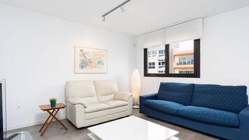 A modern living room with a white sofa, a blue sofa, a white coffee table, a floor lamp, and a painting on the wall.