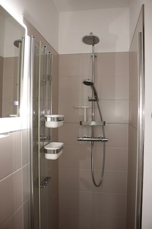 Eine moderne Duschkabine mit Glastür, Chromarmaturen und einem an der Wand befestigten Ablagebrett.