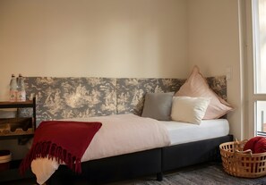 Ein Bett mit dunkelbraunem Kopfteil, einer roten Tagesdecke und einem Holznachttisch mit Flaschen.