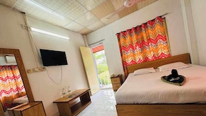Quarto de hotel com cama, mobiliário de madeira, televisão e janela com cortinas.