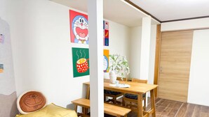 A room with a wooden bench, a dining table with chairs, a vase with flowers, and wall art. - (千本南)Doraemon House in Osaka | 4 Min to Subway | Tea Room | Easy Airport Access (Osaka)