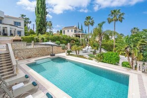 A swimming pool with lounge chairs, surrounded by palm trees and a stone wall. - Seaview Villa Selenia pool & jacuzzi in Neo Chorio (Polis Chrysochous)