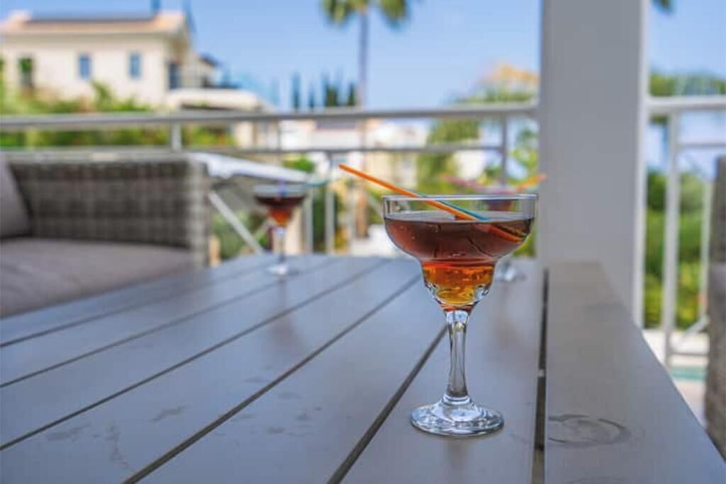 Een glas amberkleurig drankje op een houten tafel met uitzicht op een balkon.