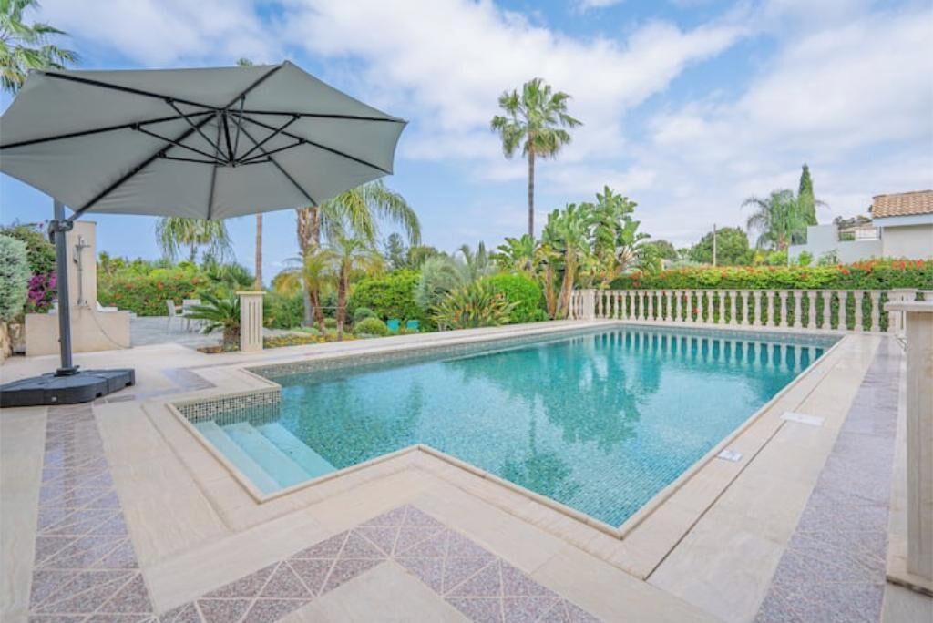 A swimming pool with a tiled deck, surrounded by palm trees and a fence.