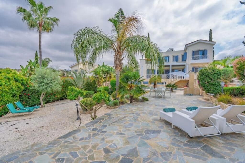 A pool area with stone flooring, lounge chairs, and palm trees.