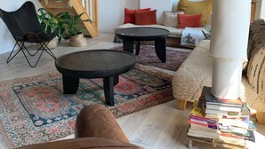 Un salon avec un escalier, une table basse, un canapé, un fauteuil, une bibliothèque et une grande plante.