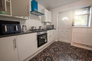 Une cuisine de taille réduite avec des meubles blancs, un four noir, une cuisinière à gaz et un four à micro-ondes.