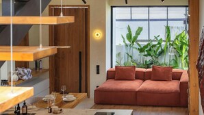 A modern living room with a sofa, a dining table, and a kitchen area with an induction cooktop. - Art Villa by Betterplace (Ubud)
