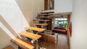 A modern interior with a wooden staircase, a kitchen area, and a seating area with a sofa. - Art Villa by Betterplace (Ubud)
