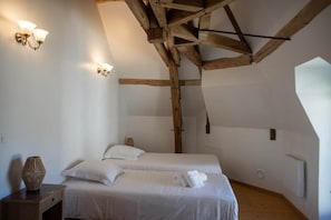 A room with two beds, wooden beams, white walls, and wall-mounted lights.