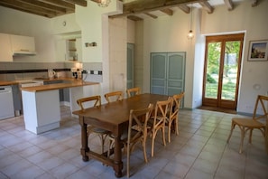 A kitchen with a wooden dining table and chairs, a built-in island, and a view of the outdoors through a glass door.