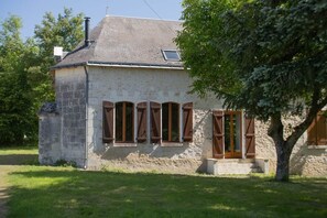 A stone building with a sloped roof, wooden shutters, and a small porch.