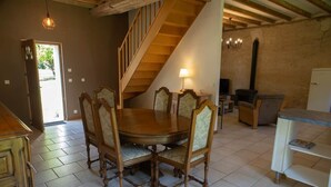 Un comedor con mesa y sillas de madera, una escalera, un televisor y un refrigerador.