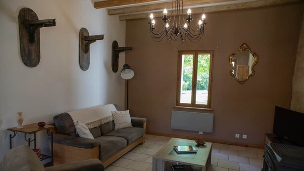 Una sala de estar con sofá, mesa de centro, televisor, chimenea, candelabro, lámpara de pared y ventana con persianas.