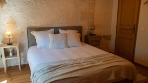 Un dormitorio con cama, una mesita de noche con lámpara, piso de madera y pared de piedra.